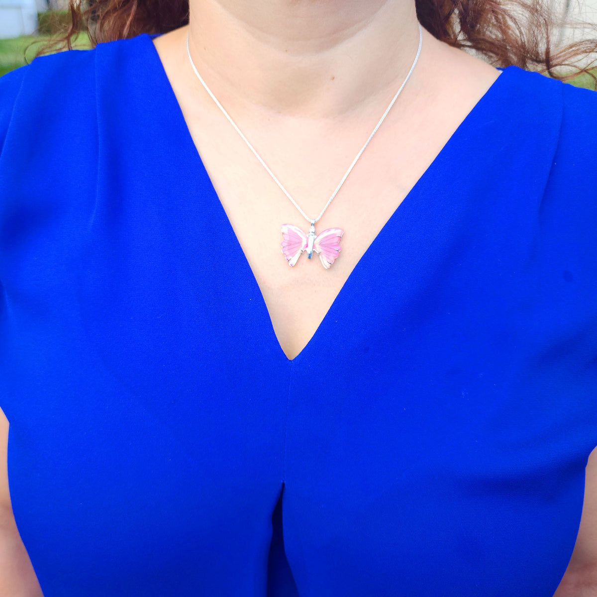 Person wearing a blue top with a butterfly pink agate pendant and silver necklace.