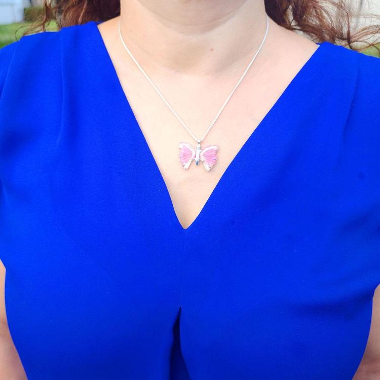 Pink natural agate butterfly pendant on a silver necklace, worn on a blue top.
