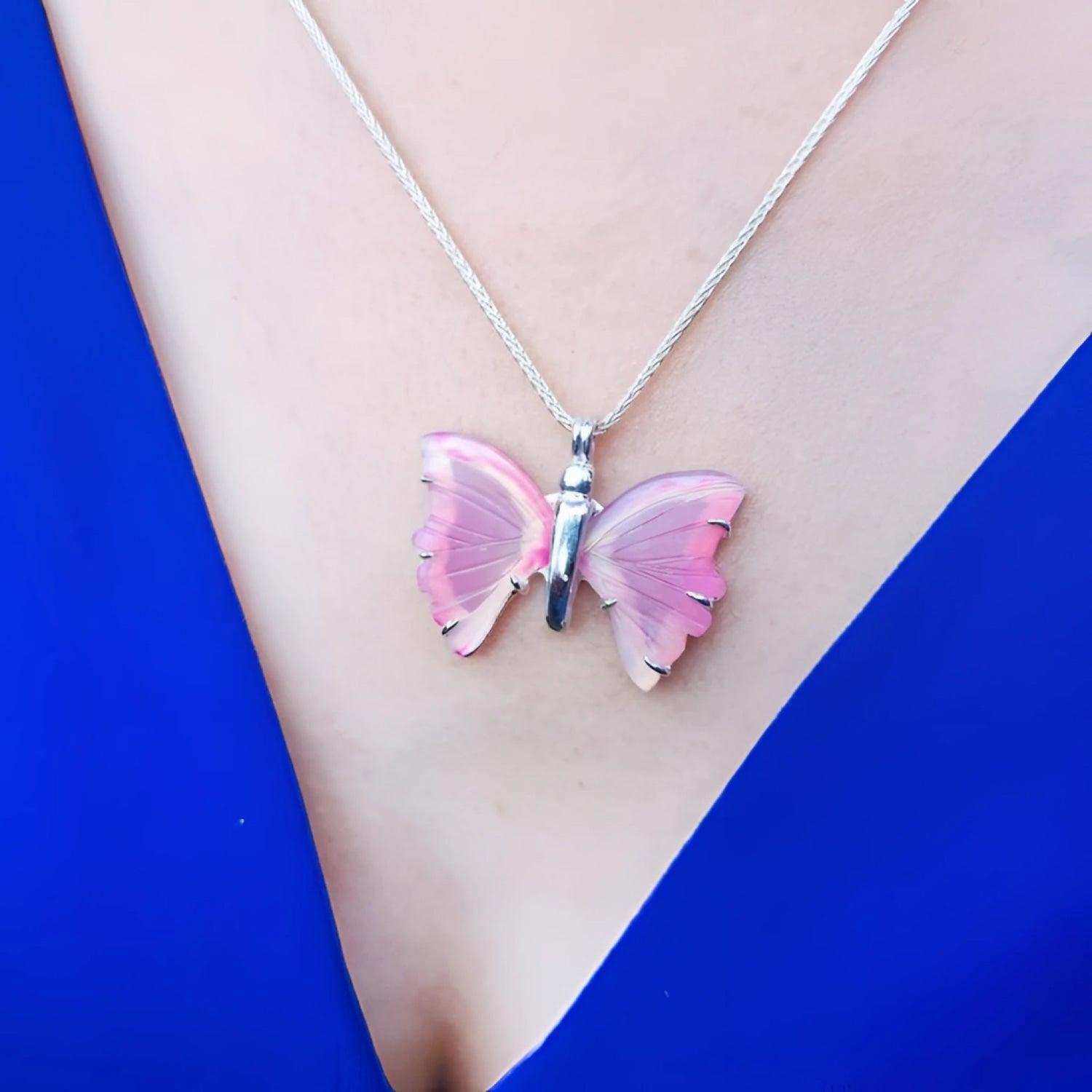 Pink natural agate butterfly pendant on a silver necklace, worn on a person in a blue top.