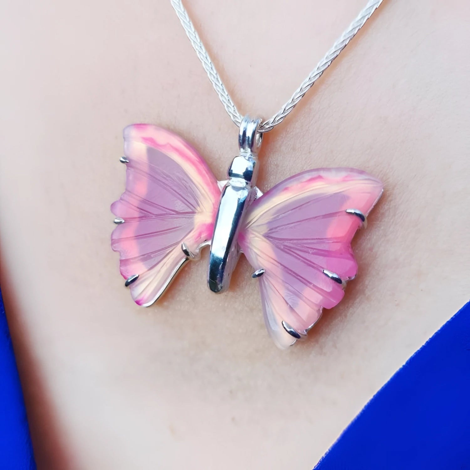 Pink natural agate butterfly pendant on a silver necklace, worn on a blue top.