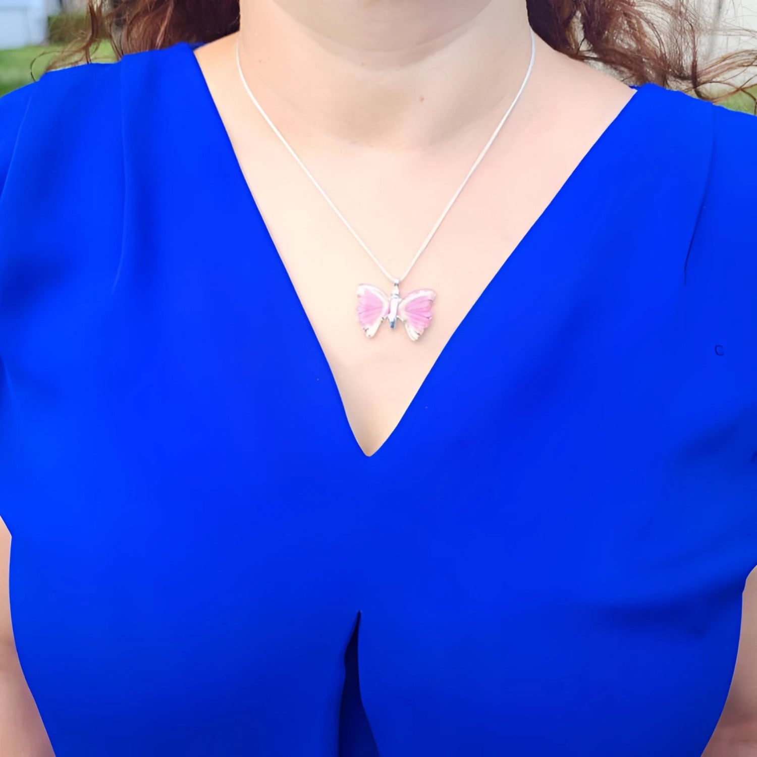 Pink natural agate butterfly pendant on a silver necklace, worn on a blue top.