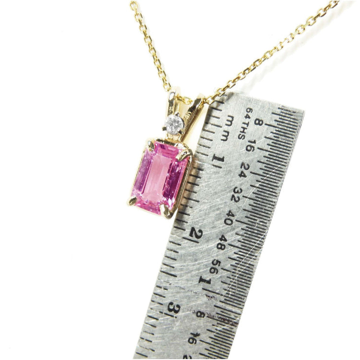 Gold necklace with a pink natural sapphire pendant next to a ruler for scale.