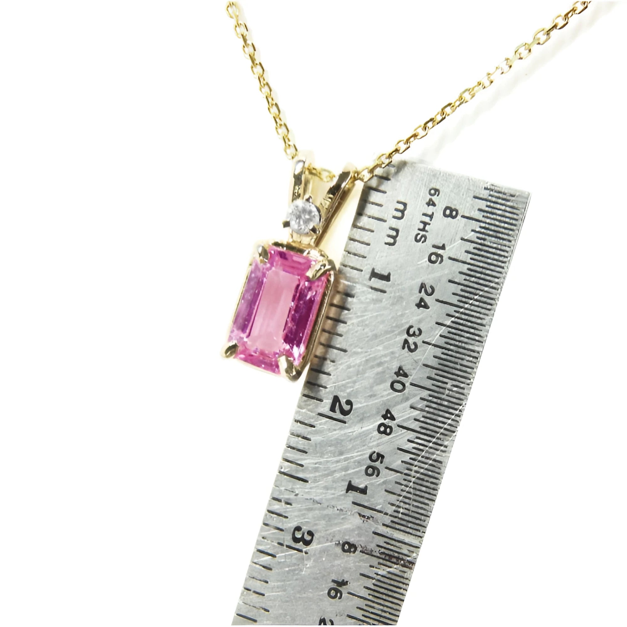 Gold necklace with a pink natural sapphire pendant next to a ruler for scale.