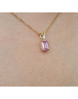 14k solid gold necklace with a natural pink sapphire pendant on a person's neck.