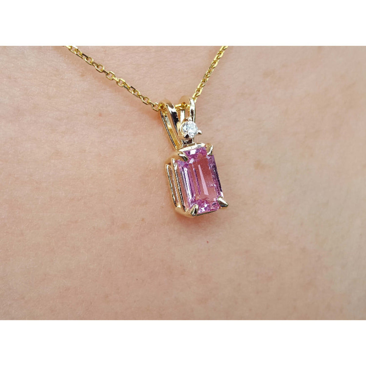 14k yellow gold necklace with a pink sapphire pendant on a skin background.