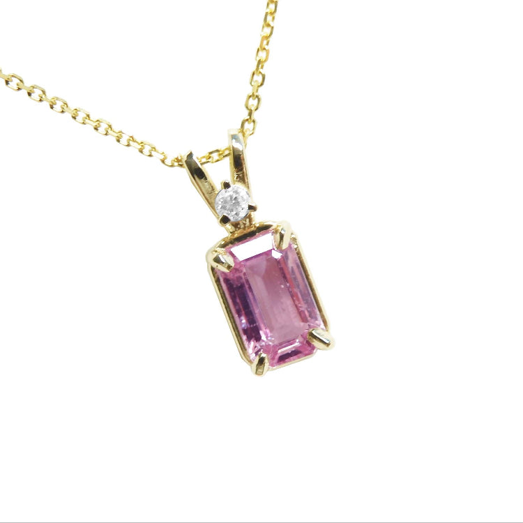 A natural emerald-cut pink sapphire and diamond pendant necklace in a prong setting, crafted in 14k yellow gold.