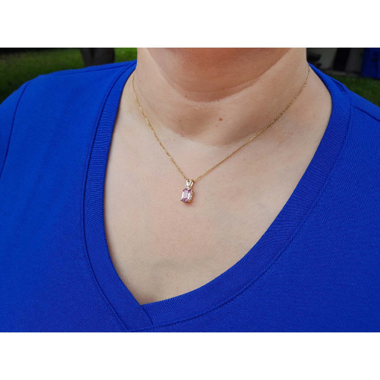 Person wearing a blue top with a 14k gold necklace featuring a pink sapphire pendant.