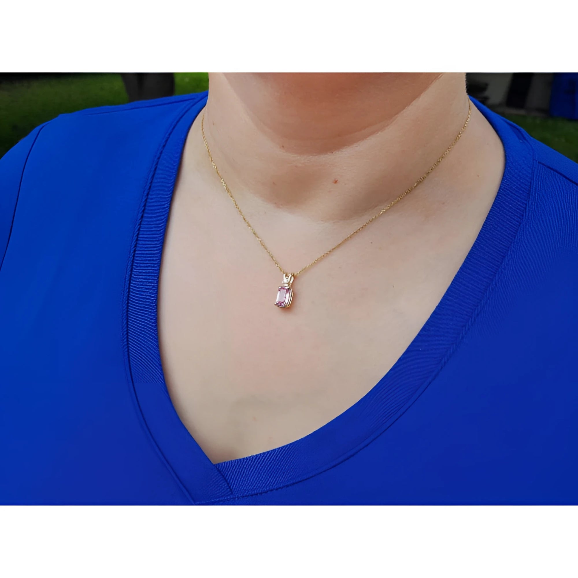 Person wearing a blue top with a 14k gold necklace featuring a pink sapphire pendant.