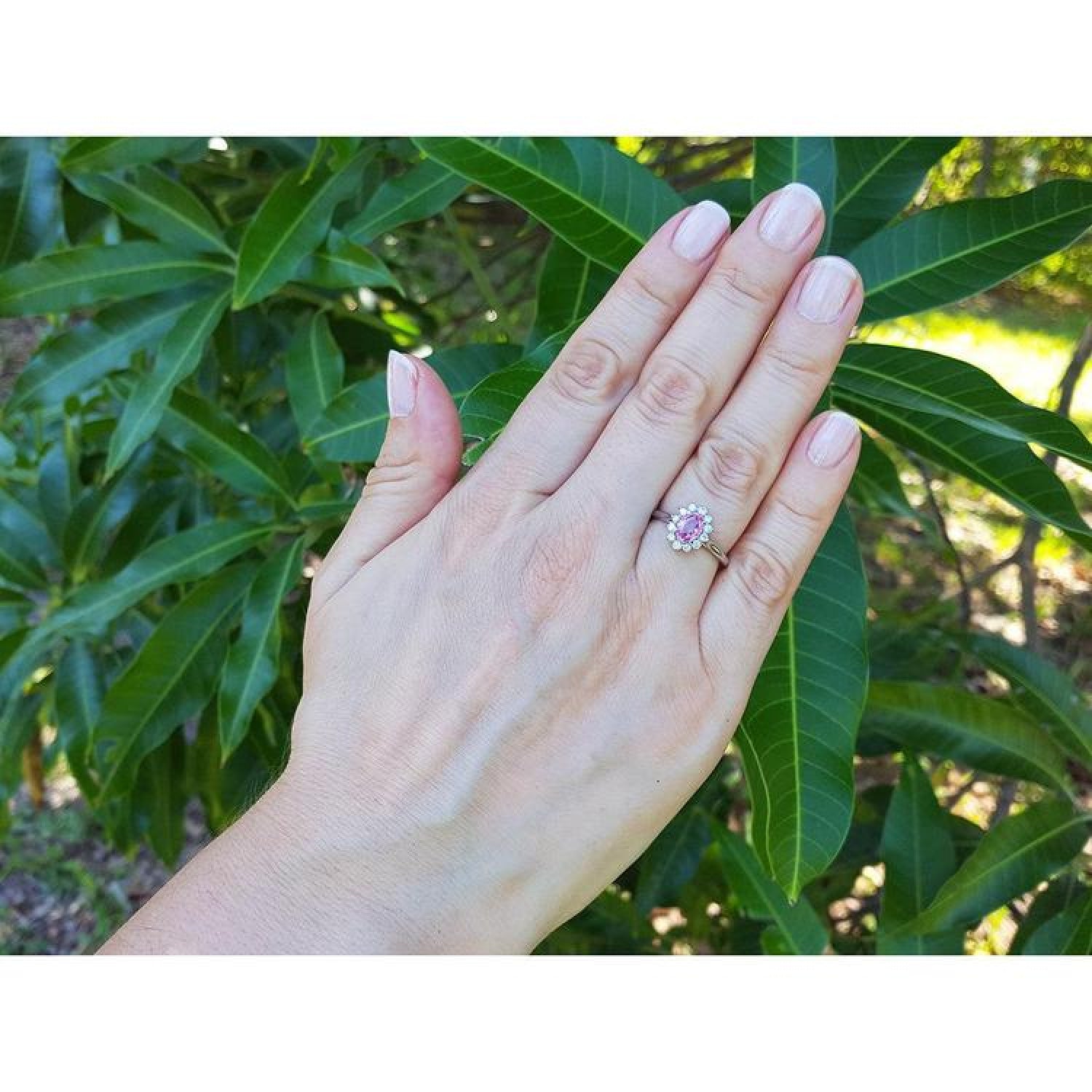 Women's 14k white gold ring with an oval pink sapphire and diamond halo on a hand.