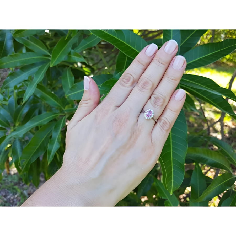 Women's 14k white gold ring with an oval pink sapphire and diamond halo on a hand.