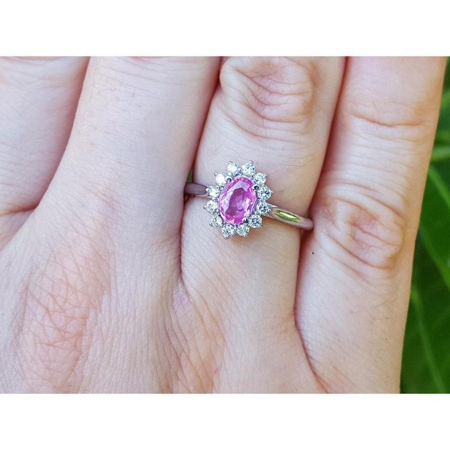 14K white gold ring with oval pink sapphire and diamond halo on a finger.