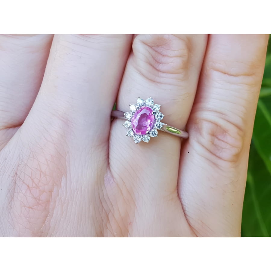 14K white gold ring with oval pink sapphire and diamond halo on a finger.
