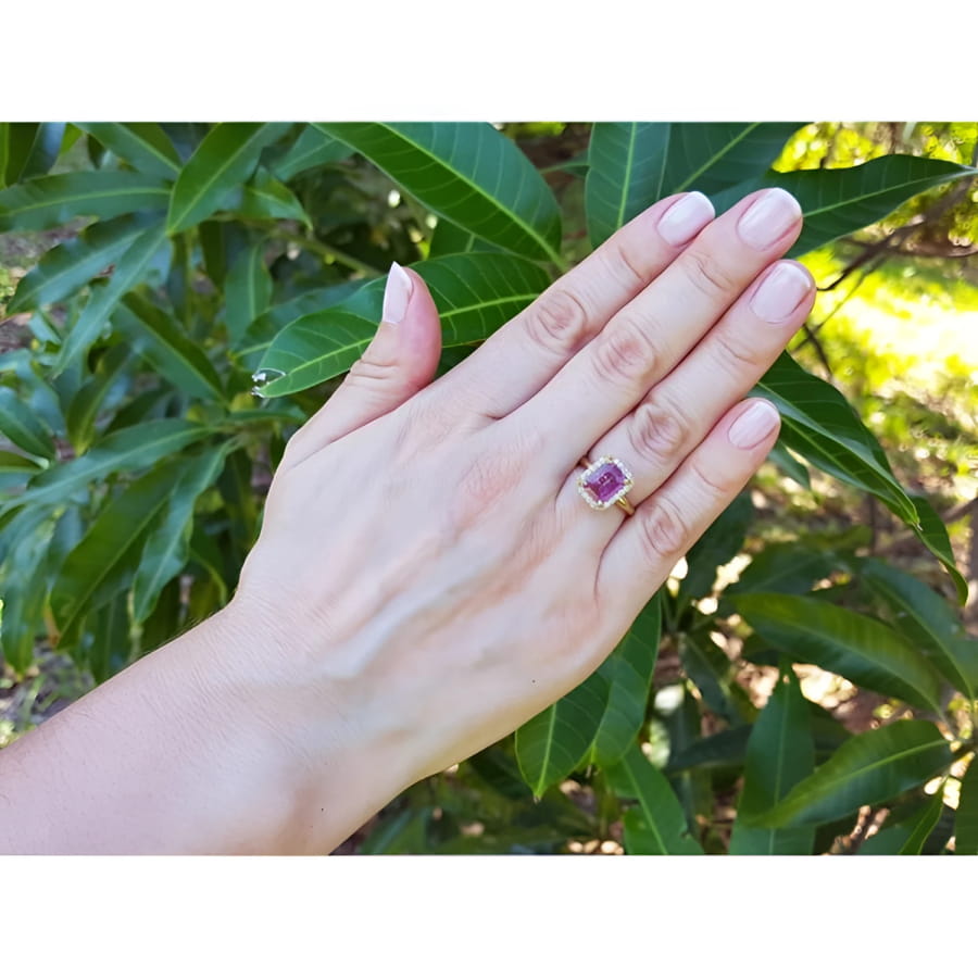 Woman's hand wearing a 14K yellow gold ring with an emerald-cut pink sapphire and diamond halo.