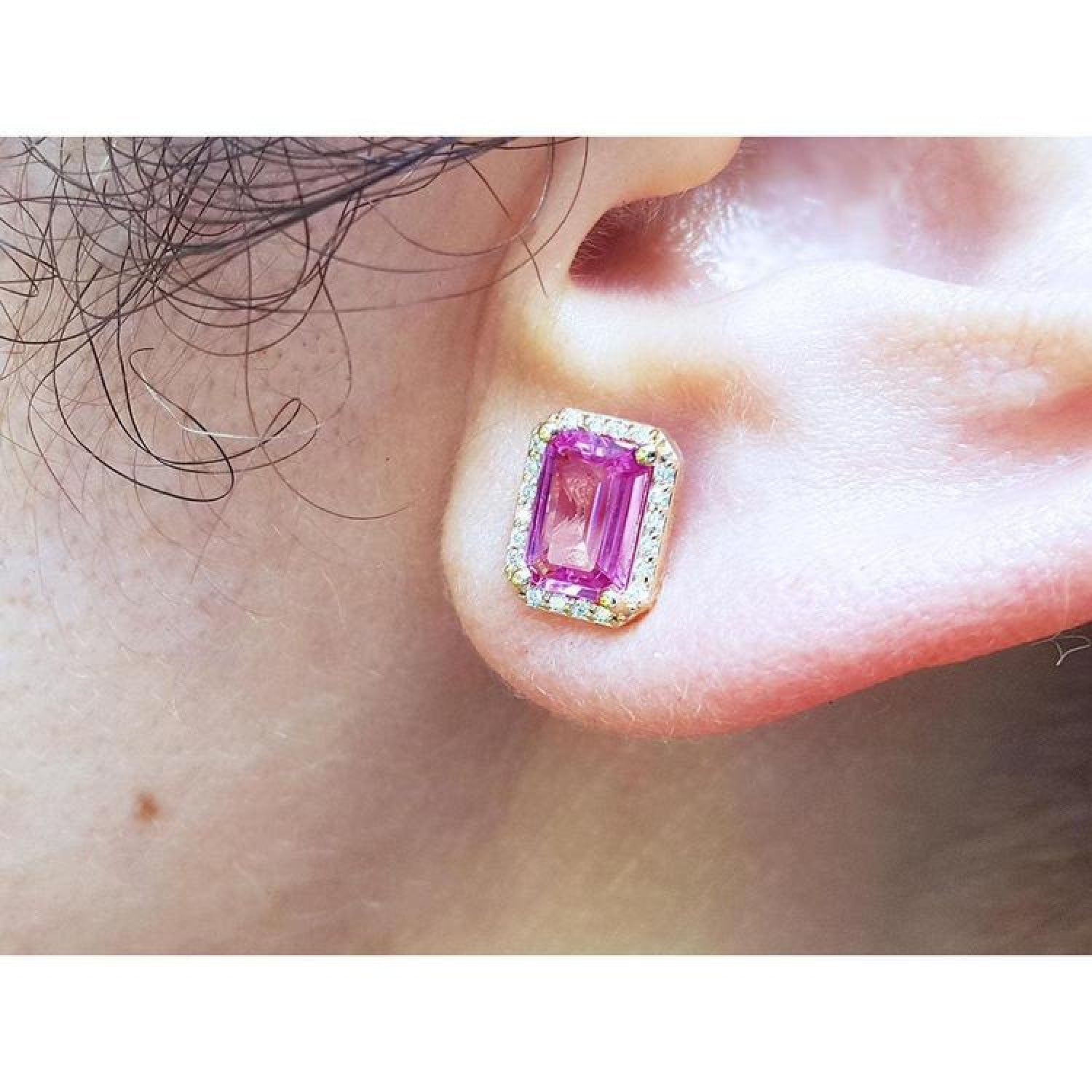 Pink sapphire emerald cut stud earring with diamond halo in 14K yellow gold on an ear.