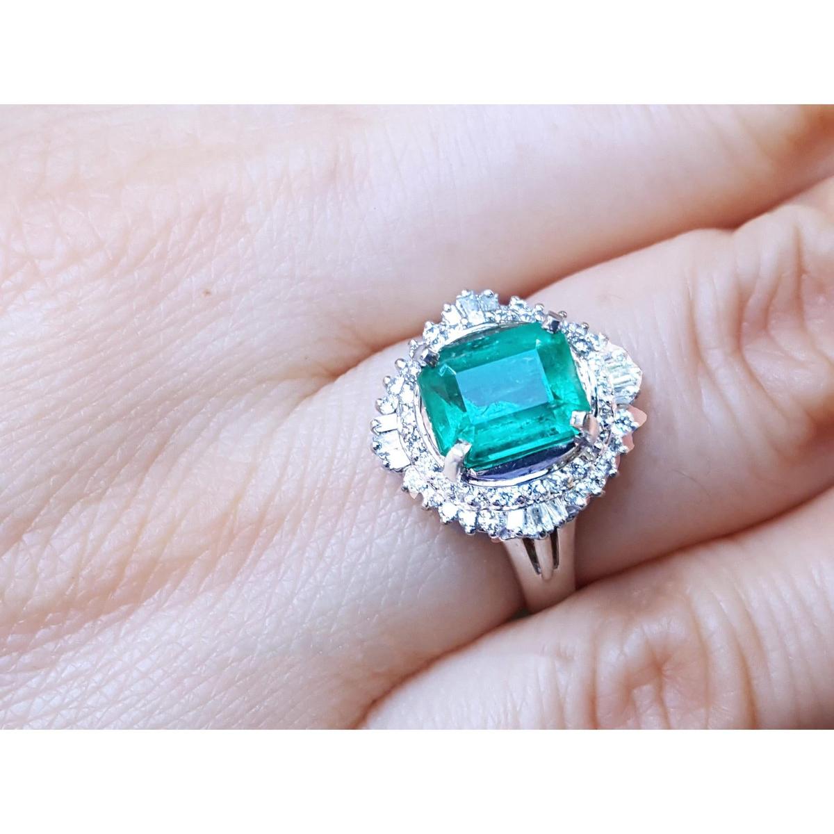 A platinum emerald ring with diamond halo on a hand.