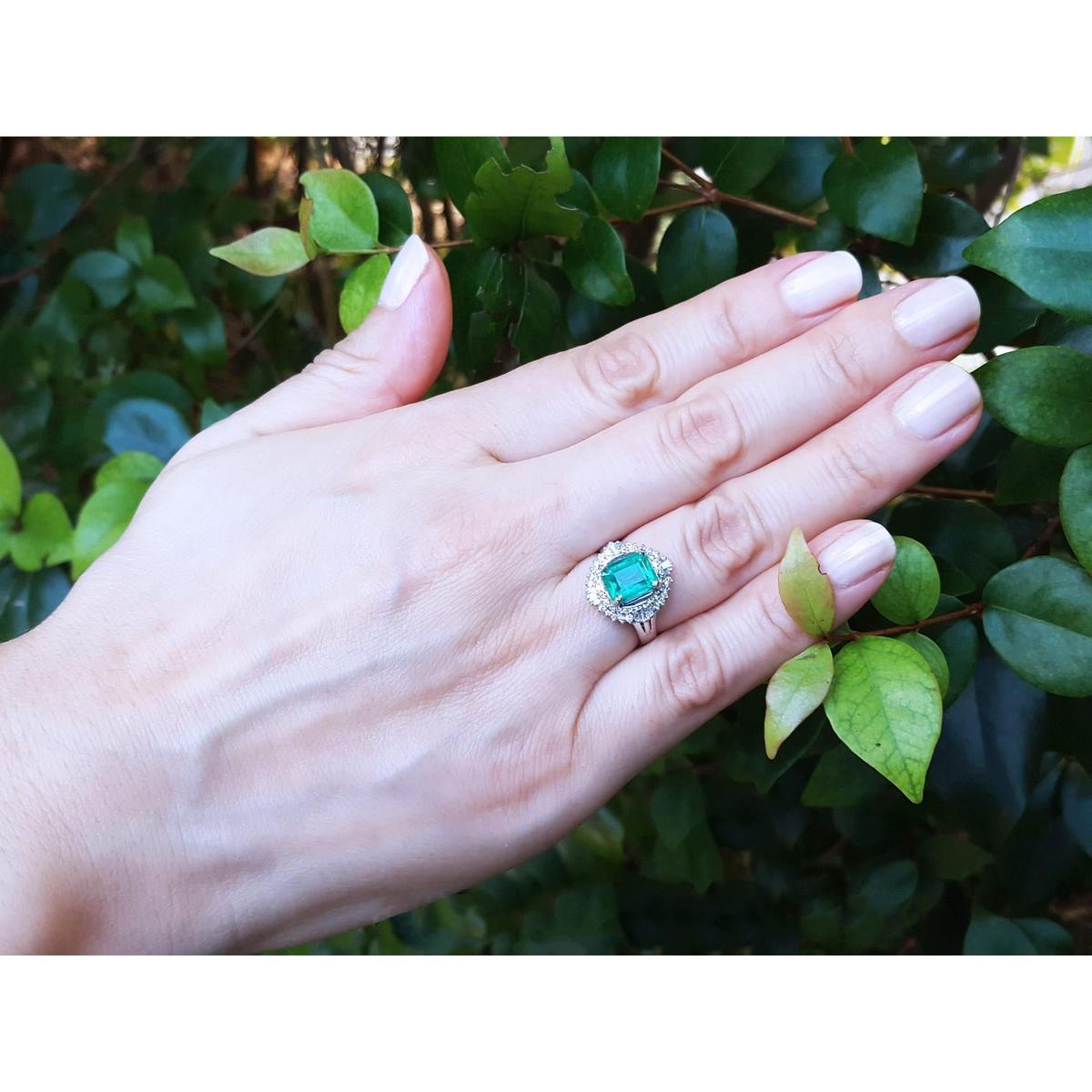 Hand wearing a ring with colombian emerald against a leafy background.