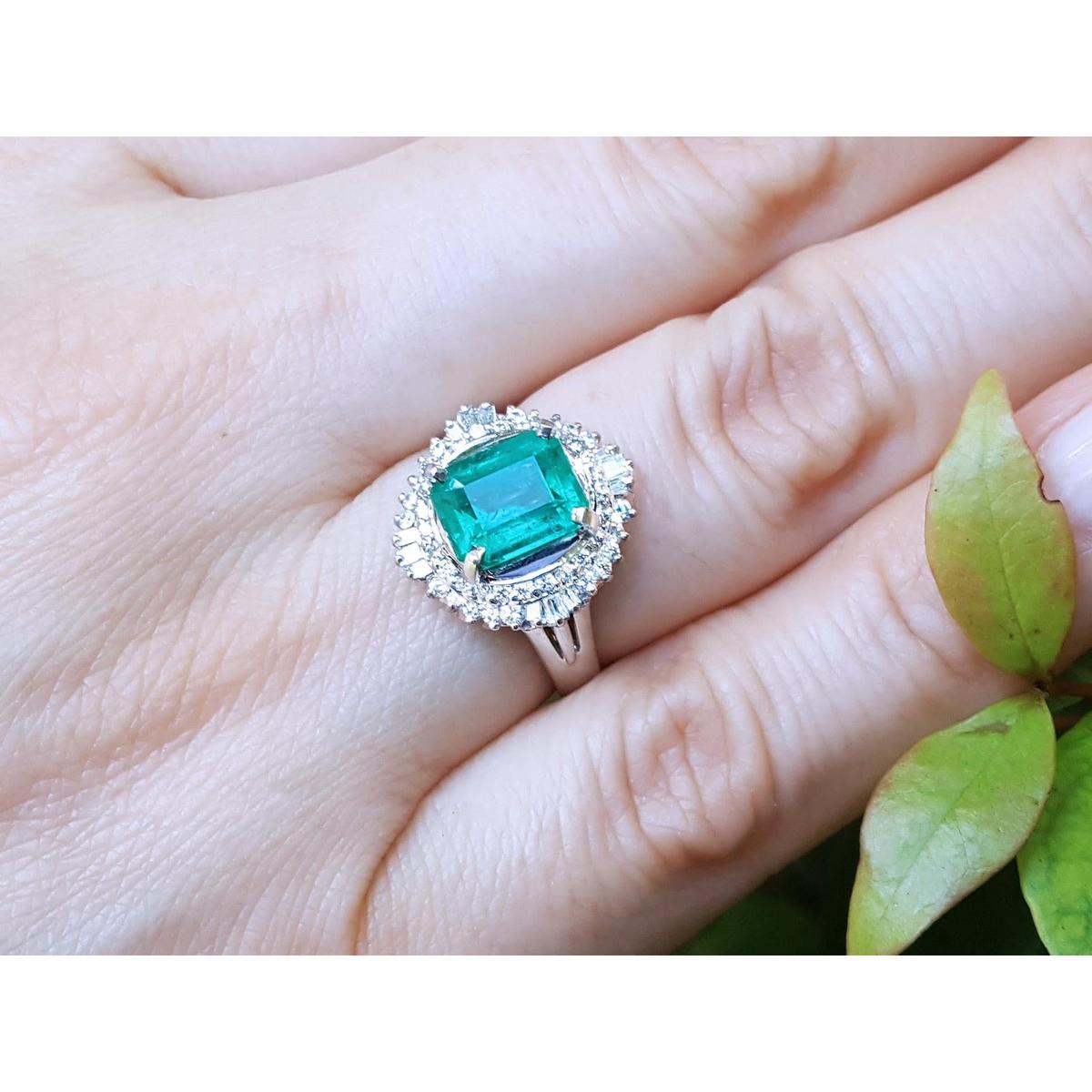 Emerald ring with diamond halo on a hand.
