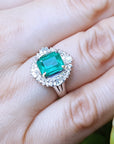 Emerald ring with diamond halo on a hand.