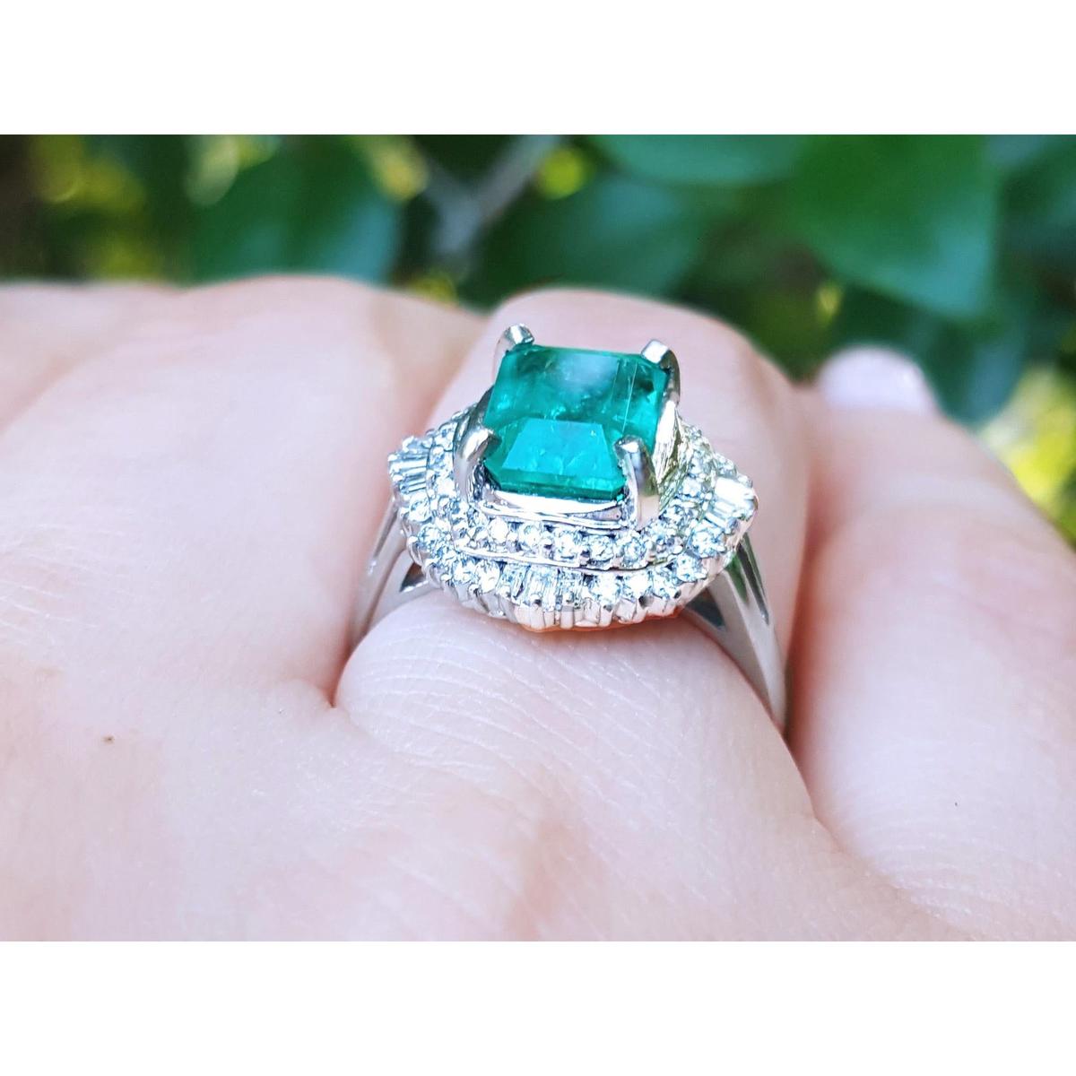 Ring with a Muzo emerald and diamond accents on a finger against a blurred natural background.