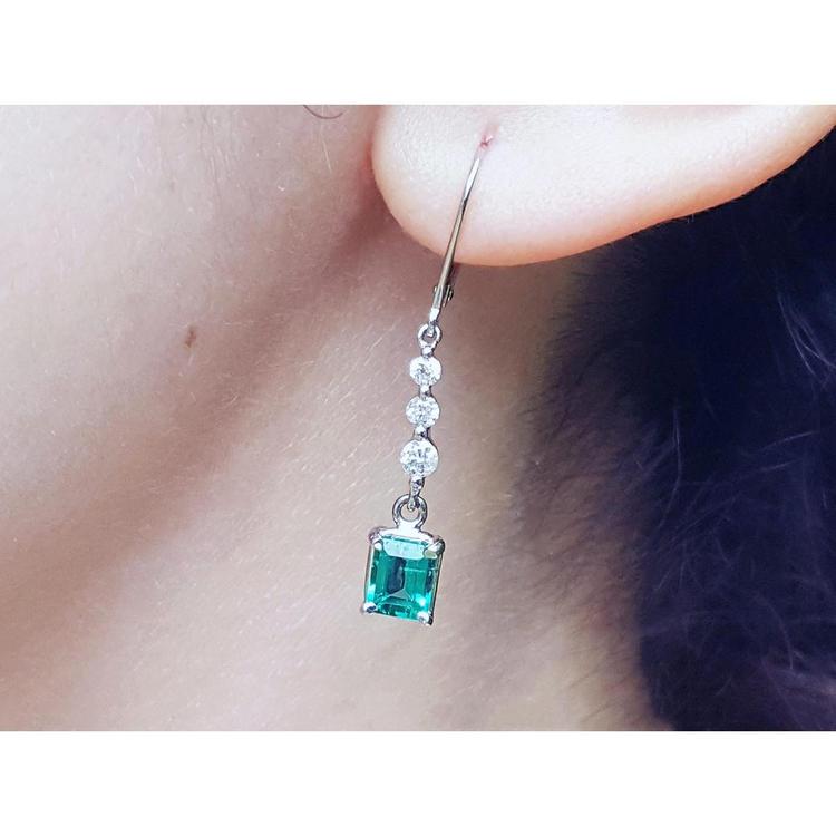 A natural Muzo colombian emerald dangle earring in white gold on an ear lobe.