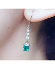 A natural Muzo colombian emerald dangle earring in white gold on an ear lobe.