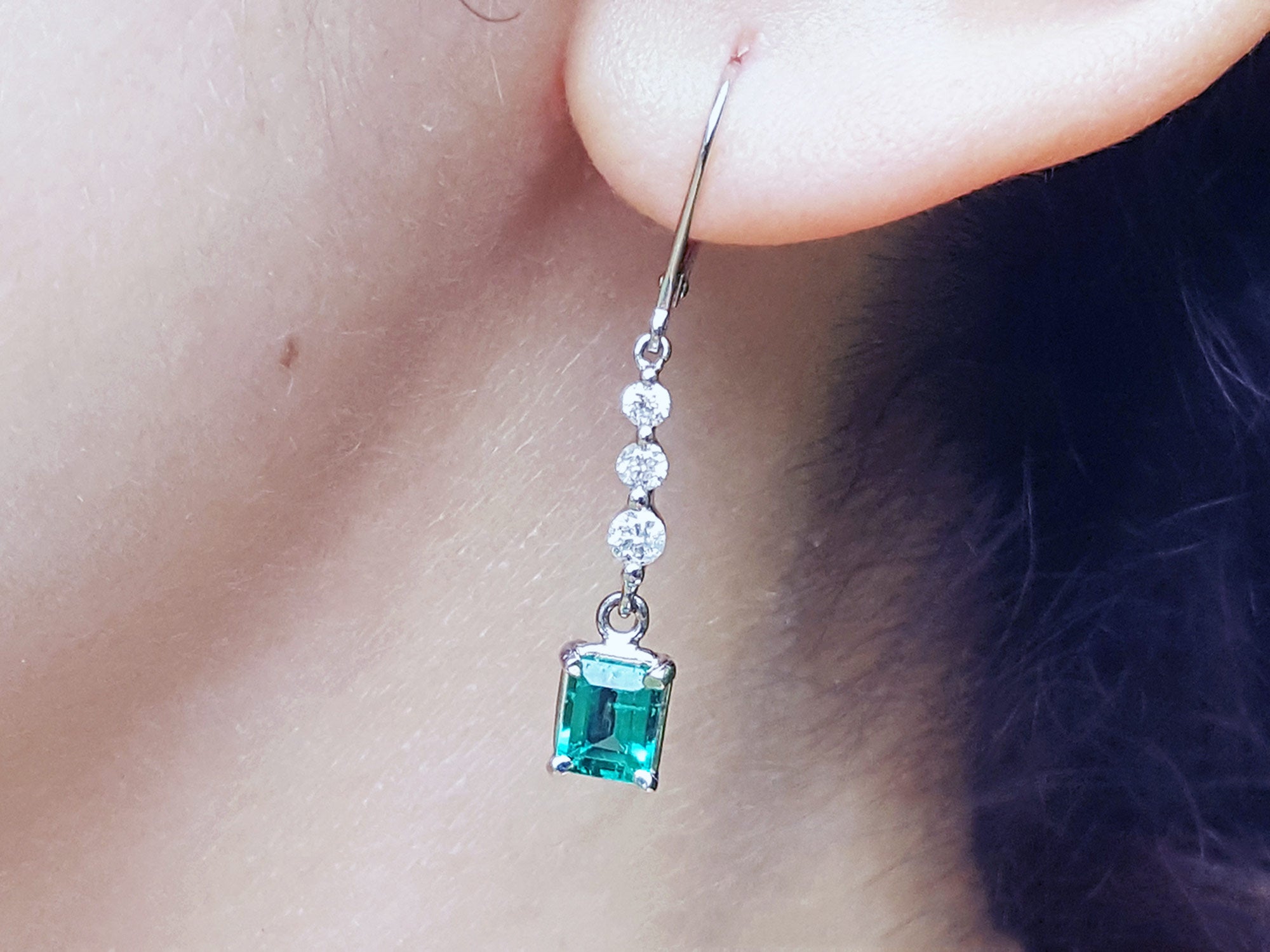 Close-up of a natural emerald dangle earring on an ear lobe.