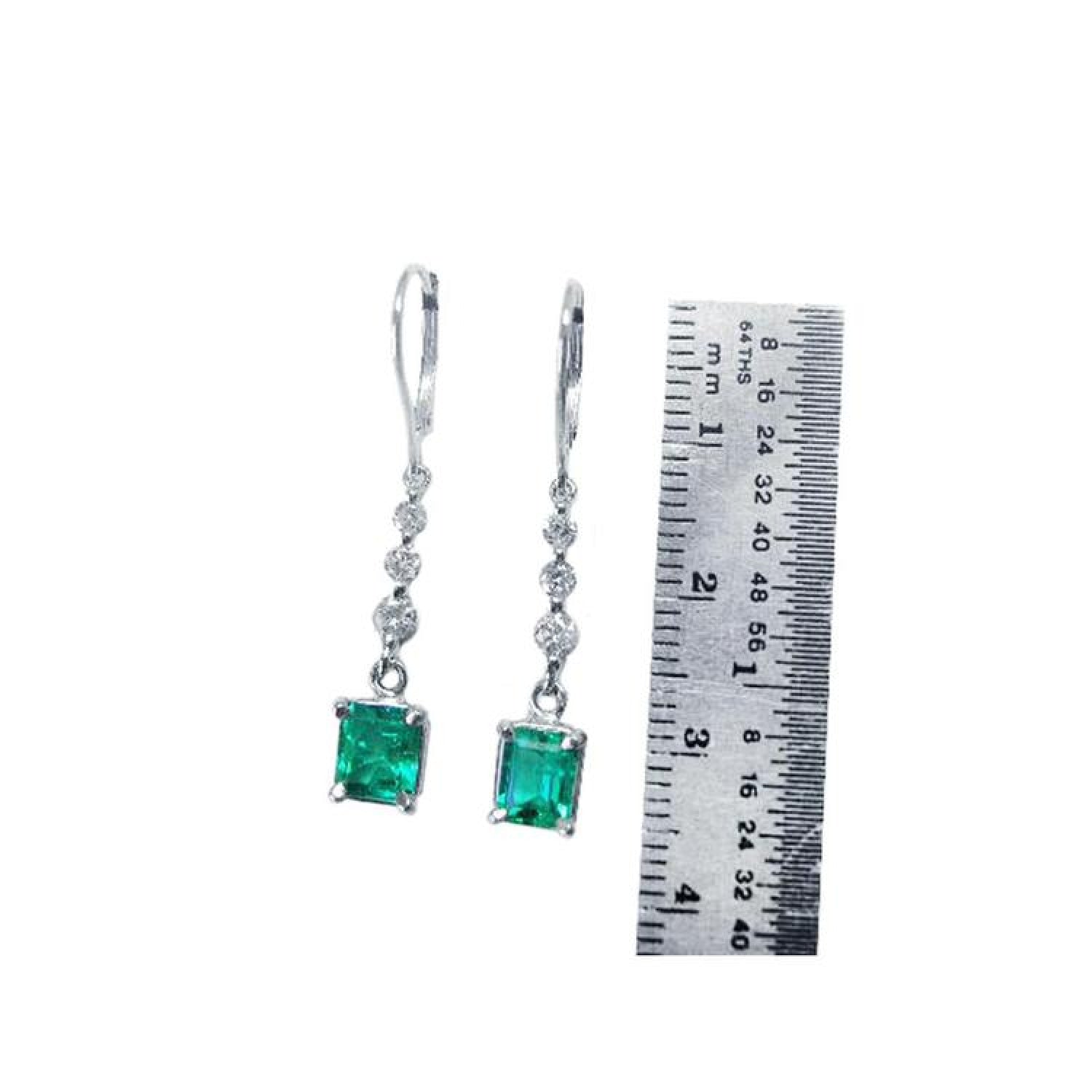 14K white gold dangle earrings with square-cut Colombian emeralds and diamond accents, next to a ruler.