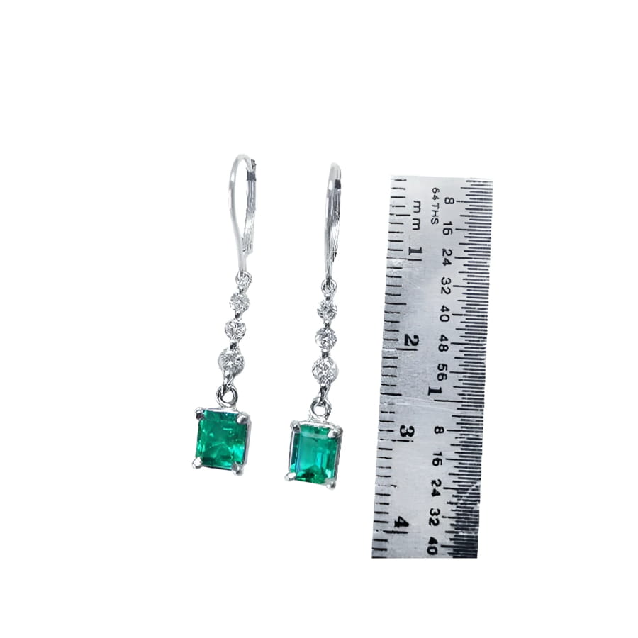 14K white gold dangle earrings with square-cut Colombian emeralds and diamond accents, next to a ruler.