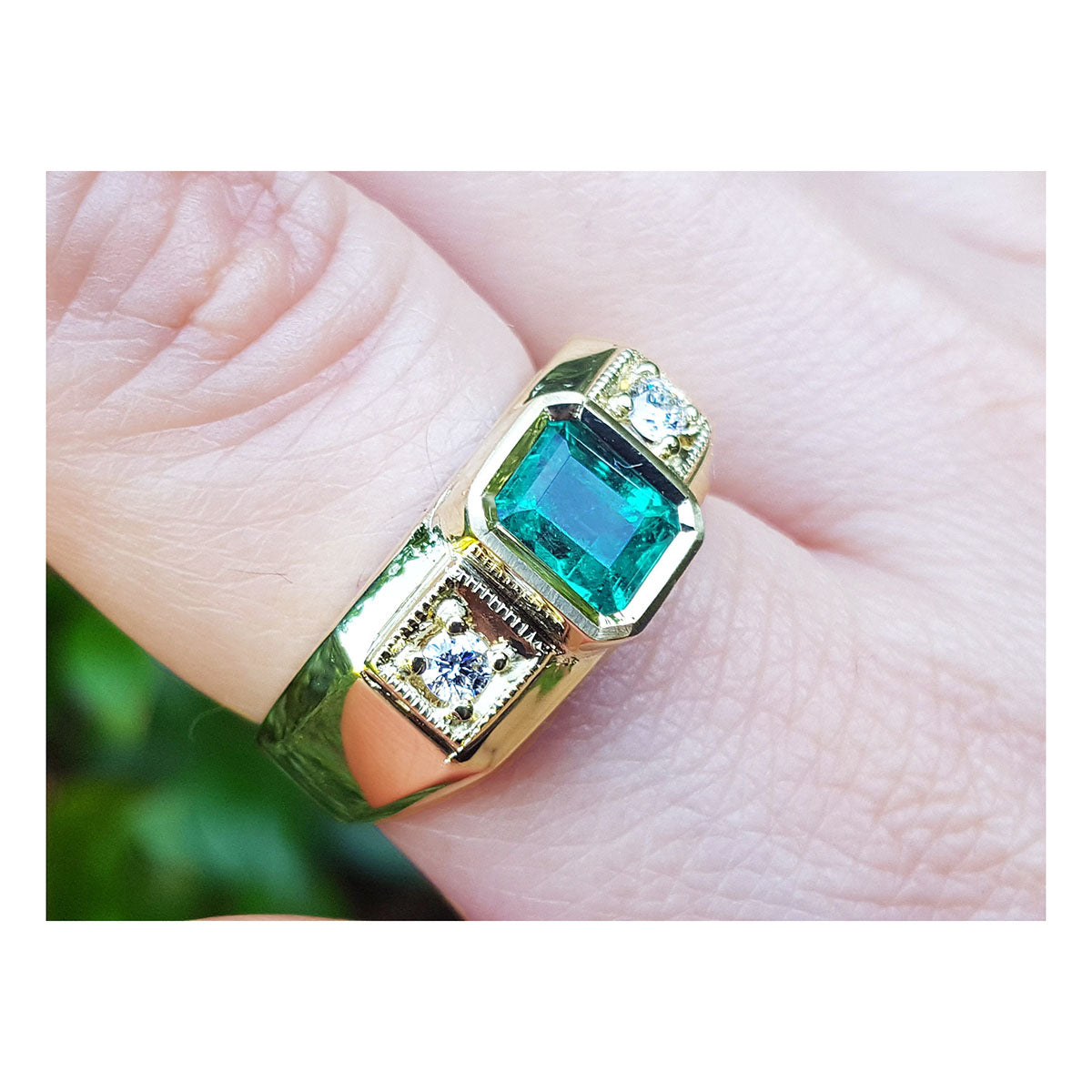 A men's gold ring with emerald and diamonds on a finger