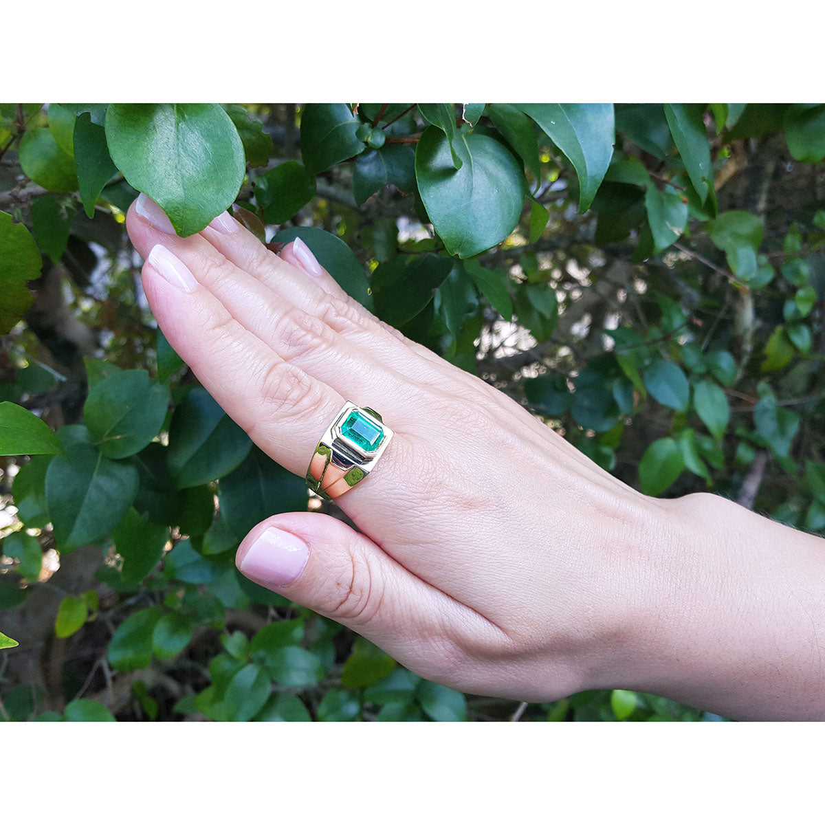 Hand wearing a natural emerald gemstone ring with a leafy background