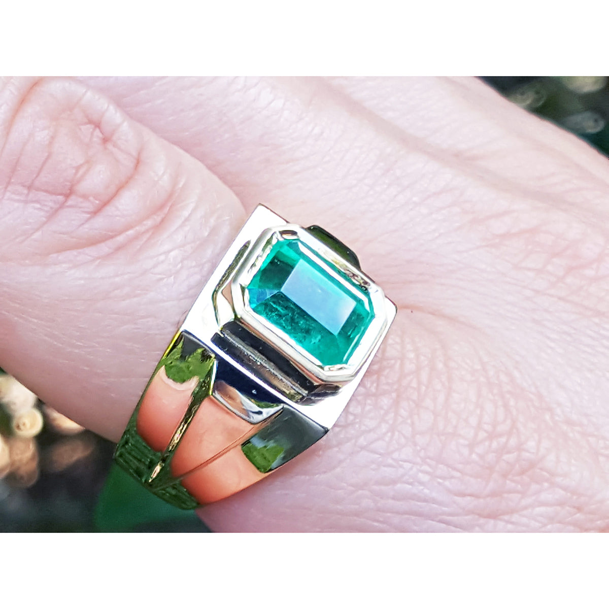 Gold ring with a bezel set solitaire emerald on a finger.