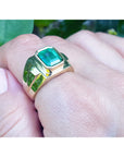 A 18k yellow gold ring with a Muzo colombian emerald on a hand against a natural background.