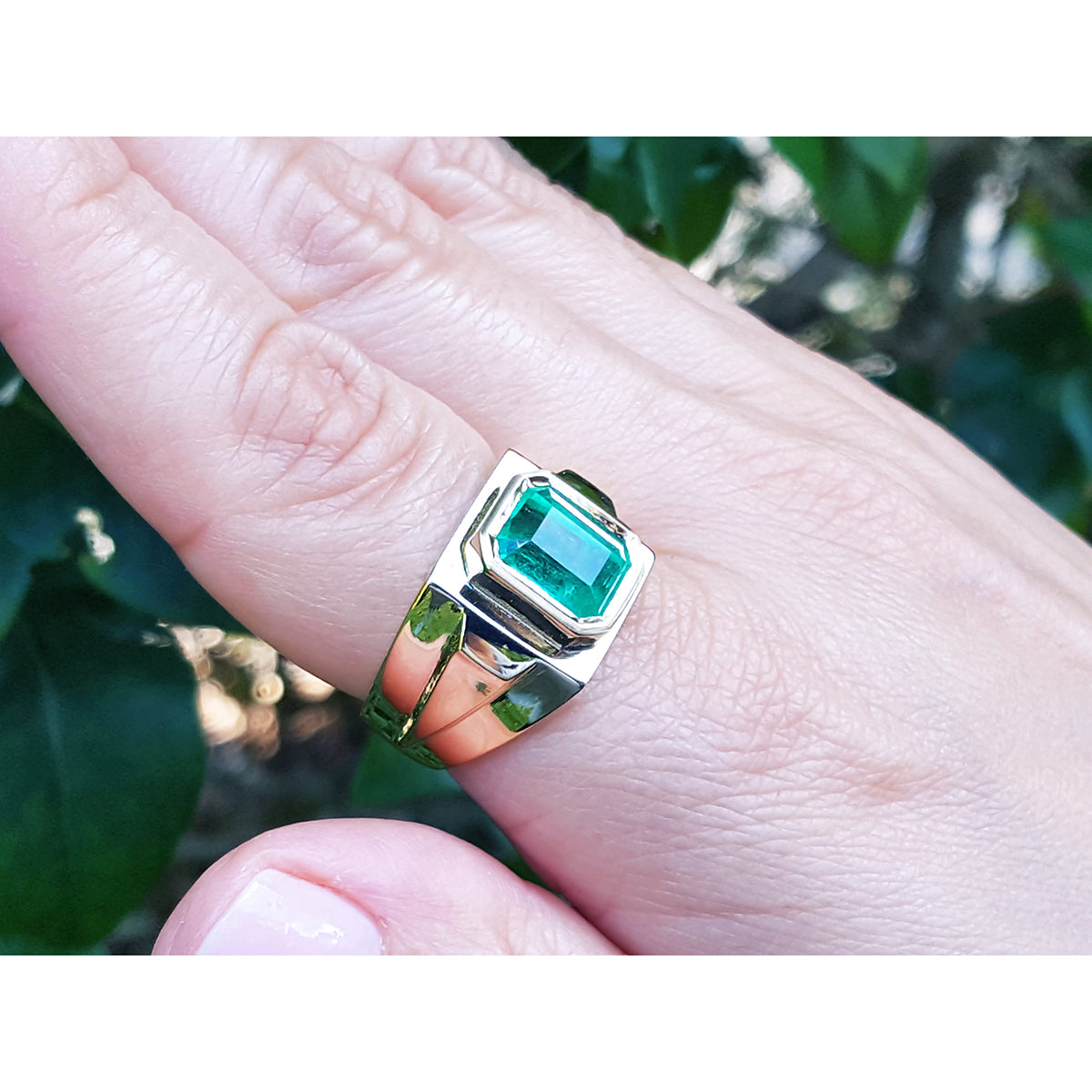 Gold ring with a emeald-cut colombian emerald on a hand against a blurred natural background.