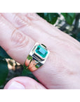 Gold ring with a emeald-cut colombian emerald on a hand against a blurred natural background.