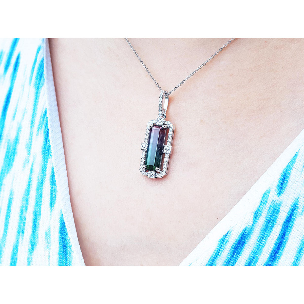 Necklace with a pendant featuring a bicolor tourmaline on a person wearing a white top with blue patterns.