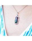 Necklace with a pendant featuring a bicolor tourmaline on a person wearing a white top with blue patterns.