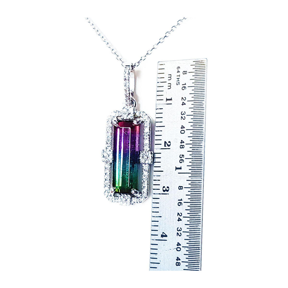 Watermelon tourmaline pendant on a chain with a ruler for scale on a white background.