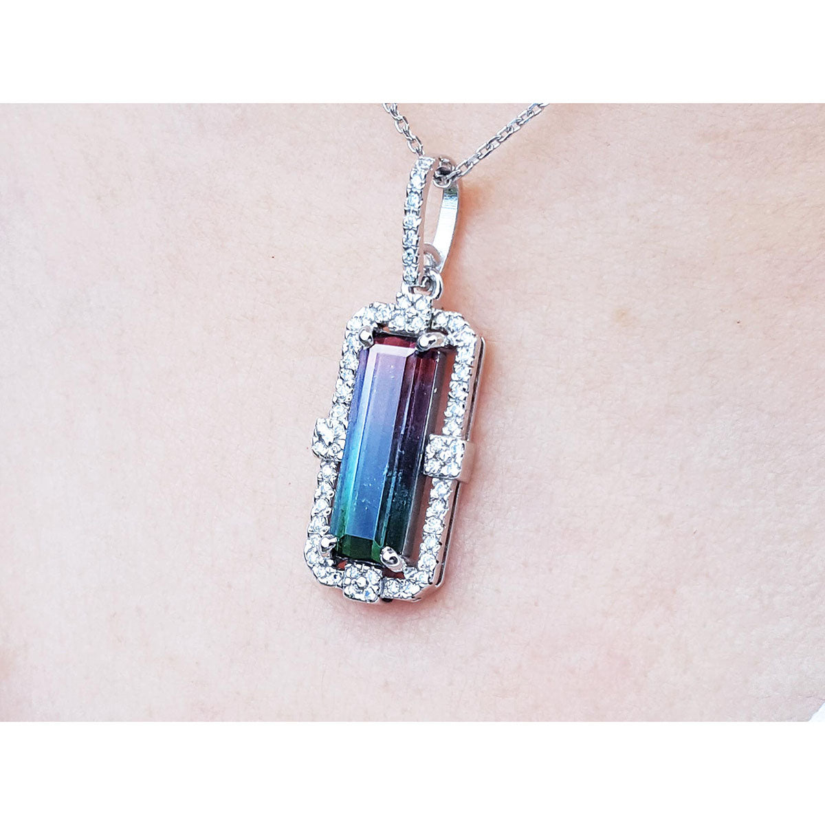A bicolor tourmaline pendant on a white gold chain against a light pink skin background.