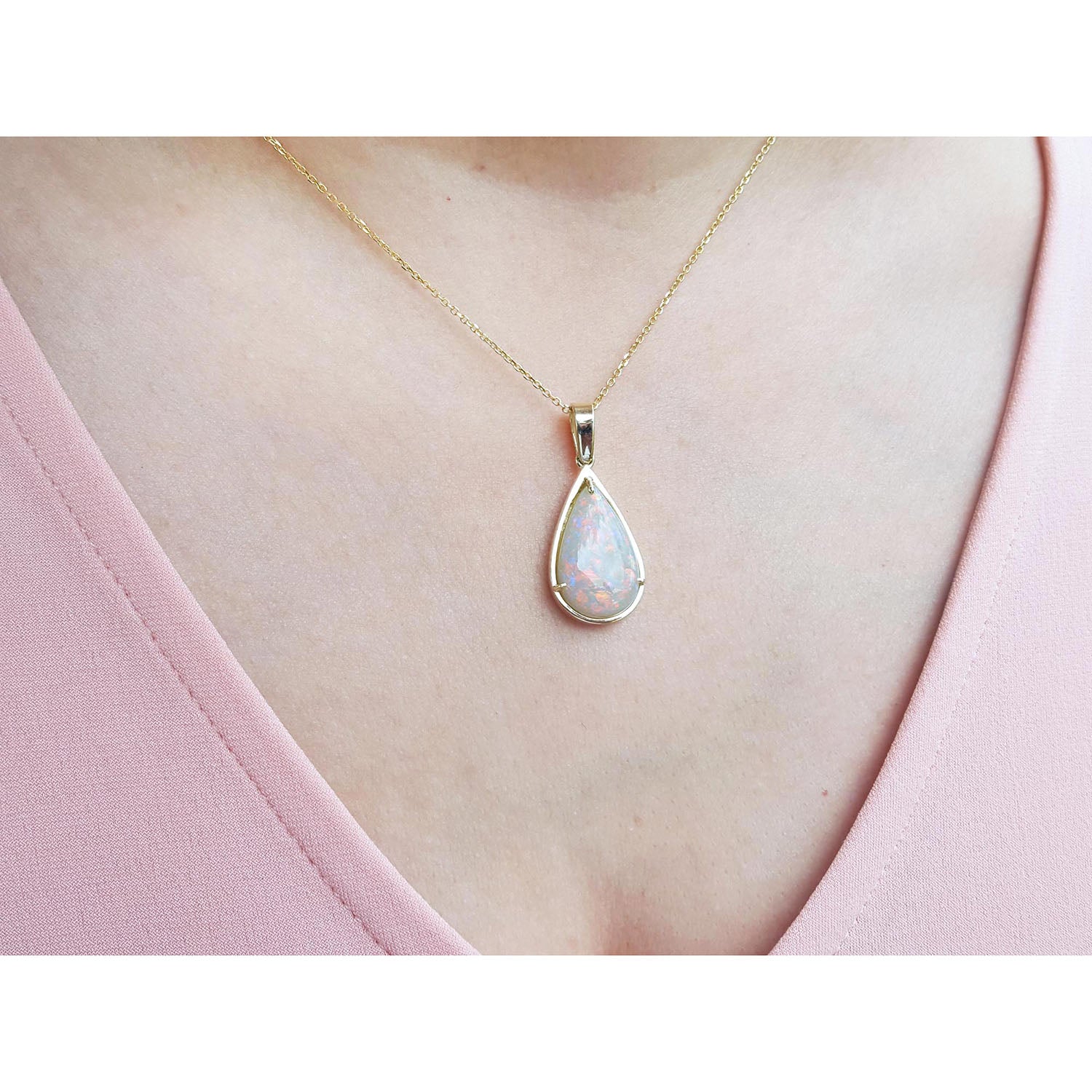 Teardrop-shaped opal pendant on a gold chain worn by a person in a pink top.