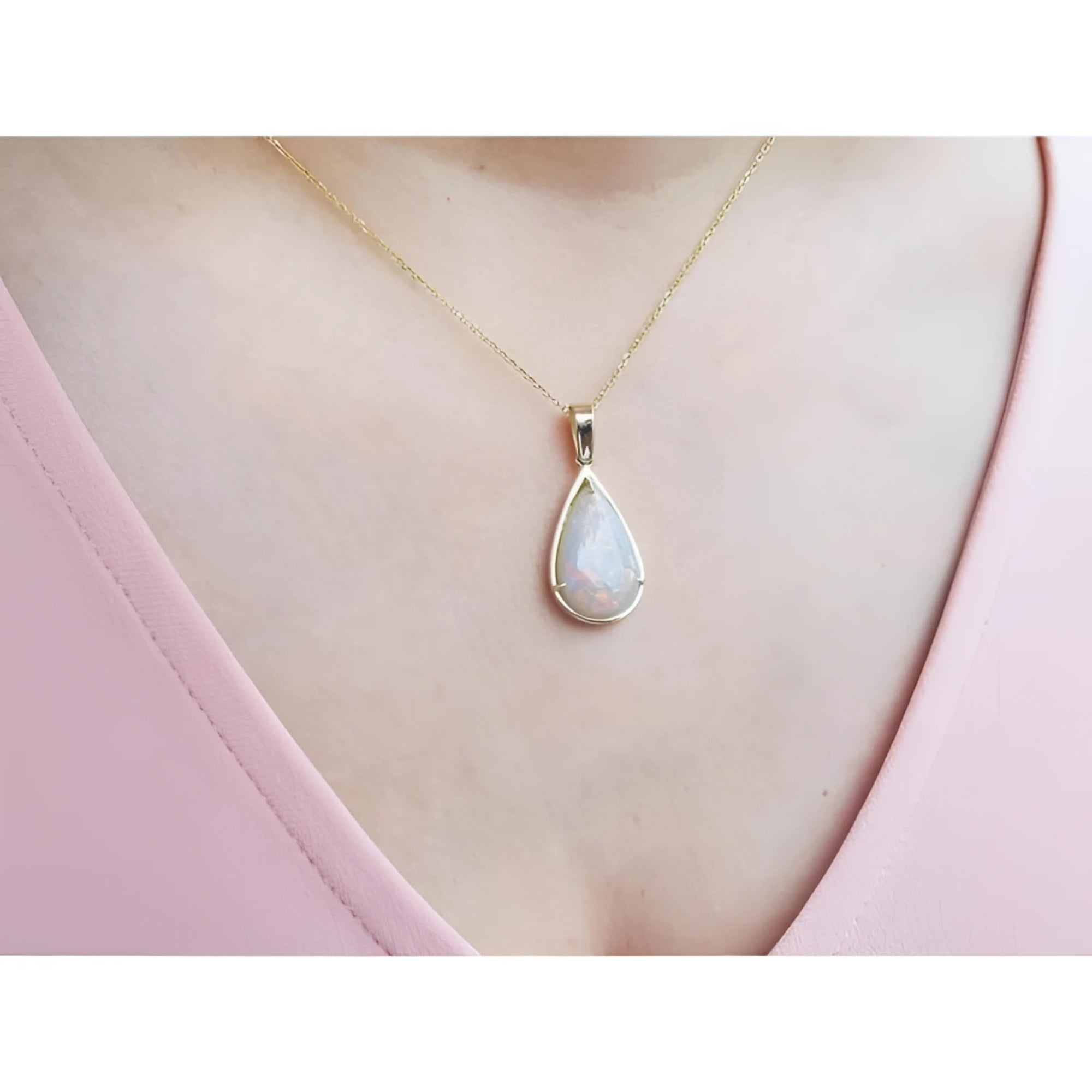 Pear-shaped Australian opal pendant with red/orange hues in 14k yellow gold on a woman's neck.