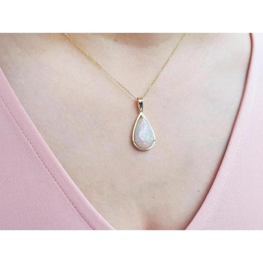 Pear-shaped Australian opal pendant with red/orange hues in 14k yellow gold on a woman's neck.