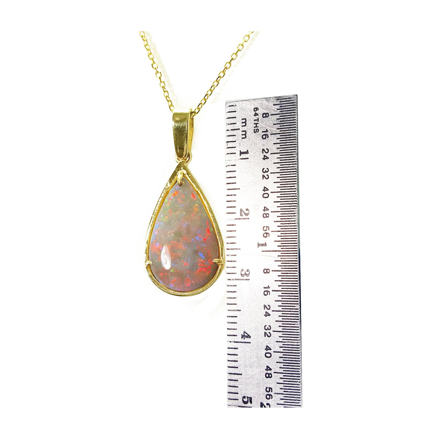 Opal pendant necklace with gold chain next to a ruler for size reference on a white background.