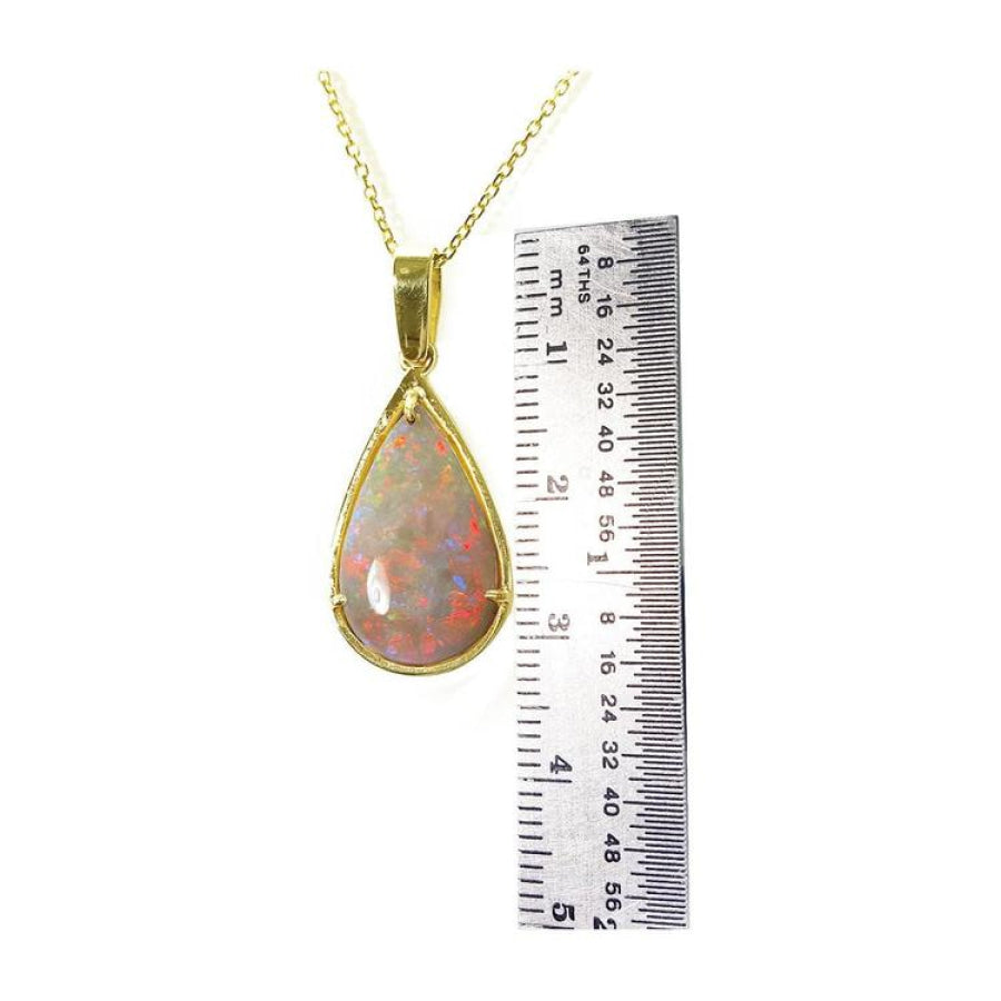 Pear-shaped Australian opal pendant with red/orange fire, set in 14k yellow gold, next to a ruler.