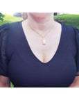 Person wearing a black top with sheer sleeves and a natural opal necklace outdoors.