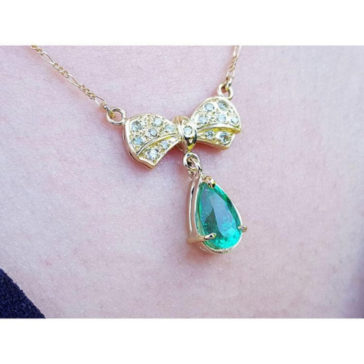 18K yellow gold bow-tie necklace with pave diamonds and a dangling pear-shaped emerald.