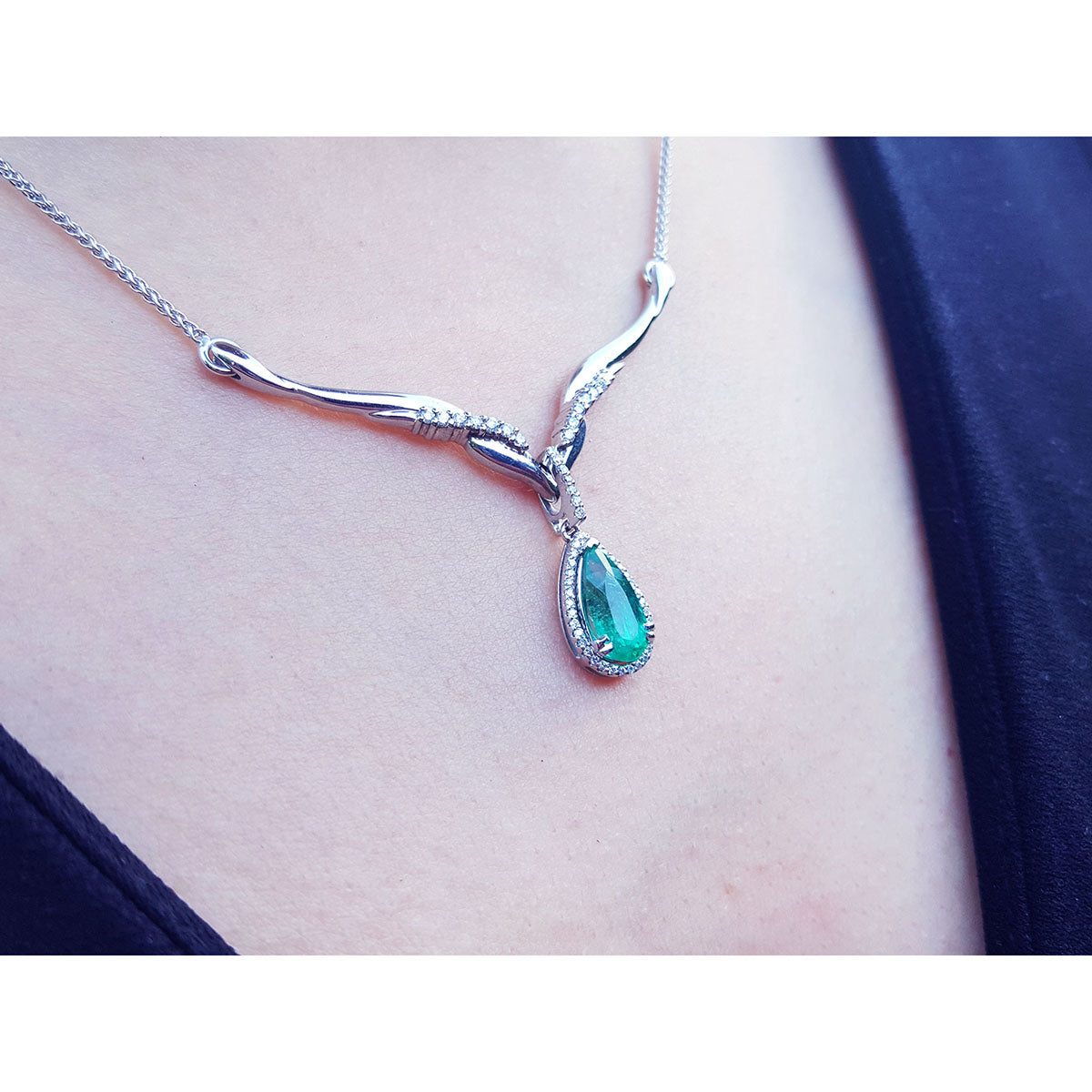 A right-side view of a white gold necklace with an emerald gemstone halo diamond pendant on a person&#39;s neck