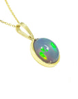 Right side profile view of a opal pendant with gold setting on a white background.