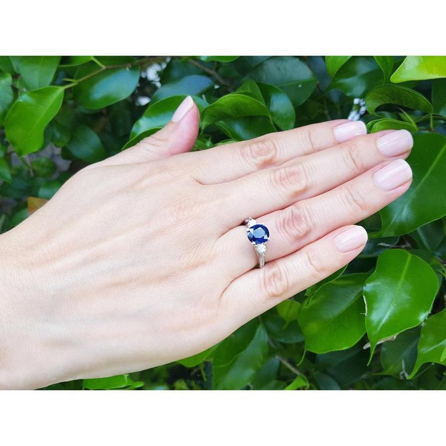 Woman's hand wearing a 14K white gold ring with a deep blue oval sapphire and side diamonds.