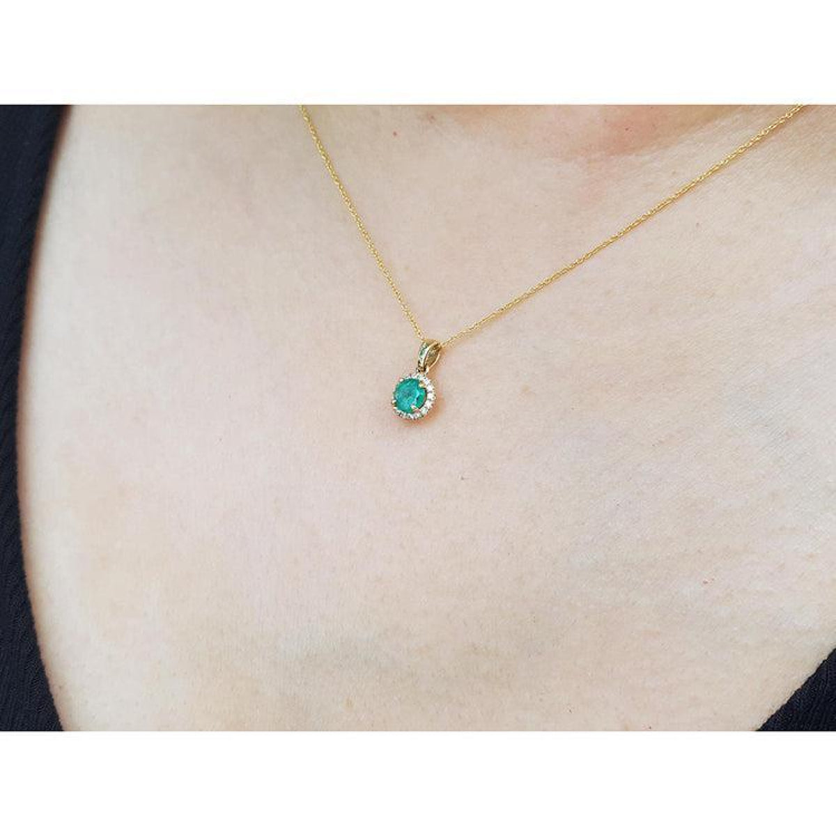 Petite round deep green Colombian emerald necklace with halo diamonds in 14k yellow gold.