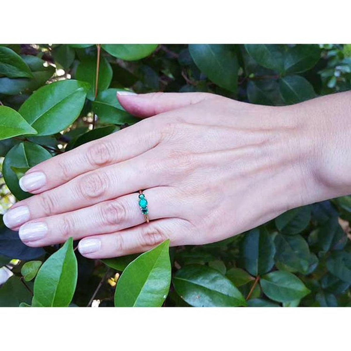 Hand wearing a round cut three stone emerald ring, 0.62 cttw, in white and yellow gold.
